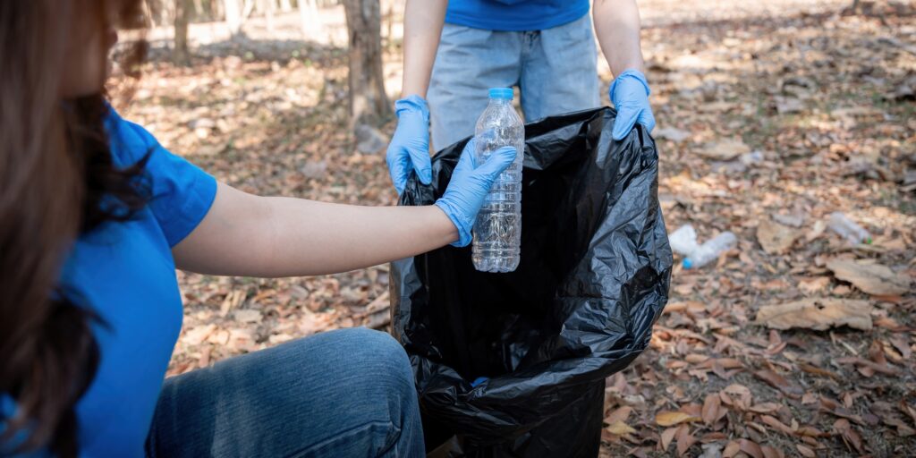 Young people friend volunteer collecting garbage plastic bottles to trash bags. environmental care